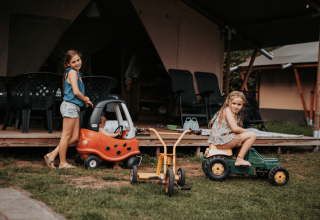 Twee meisjes spelen met speelgoedvoertuigen bij een tent op Camping Emmen vakantiepark in Drenthe, Nederland.