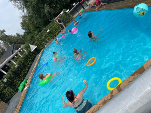 Children and adults swim and play in an outdoor pool with floaties at Camping Emmen in Drenthe, Netherlands.