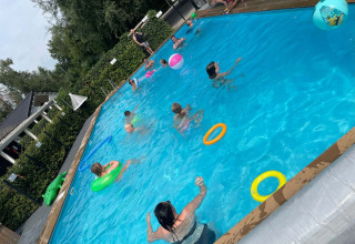 Children and adults swim and play in an outdoor pool with floaties at Camping Emmen in Drenthe, Netherlands.
