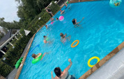 Børn og voksne leger i en udendørs swimmingpool med oppustelige legetøj på Camping Emmen i Drenthe, Holland.