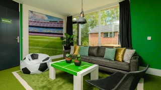 Soccer-themed living room at FC Mölke Stadium Lodge, Holiday Park Mölke, Netherlands, with green decor and mural.