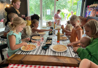 Kinderen versieren pannenkoeken samen aan tafel tijdens een activiteit op Camping Emmen in Drenthe, Nederland.