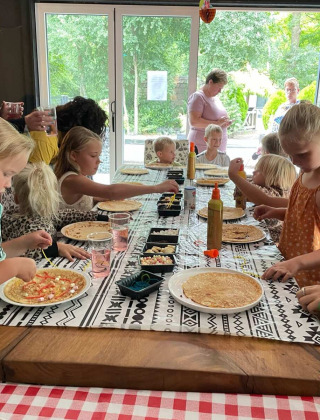 Børn laver deres egne pandekager ved et langt bord under en aktivitet på Camping Emmen i Drenthe, Holland.