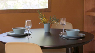 Ronde zwarte eettafel met twee plekken, blauwe kommen, wijnglazen en bloemen in een safaritent.