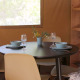 Round black dining table with two place settings, blue bowls, wine glasses, and flowers in a safari tent.