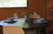 Round black dining table with two place settings, blue bowls, wine glasses, and flowers in a safari tent.