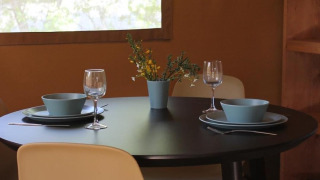 Zwarte ronde eettafel met twee dekken, blauwe kommen, wijnglazen en bloemen in een safaritent.