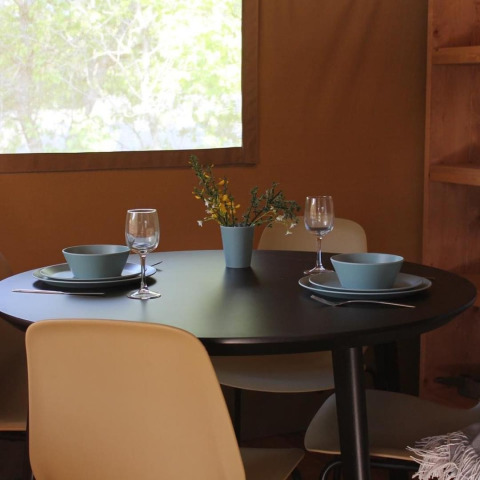 Round black dining table with two place settings, blue bowls, wine glasses, and flowers in a safari tent.