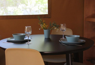 Mesa de comedor redonda y negra con dos cubiertos, cuencos azules, copas de vino y flores en una tienda safari.