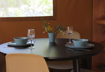 Tavolo rotondo nero apparecchiato per due, ciotole blu, calici da vino e fiori in una tenda safari.