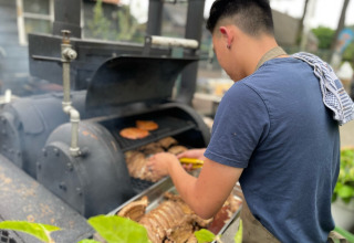 Un uomo griglia carne su un grande barbecue all'aperto a Camping Emmen, un parco vacanze a Drenthe, Paesi Bassi.