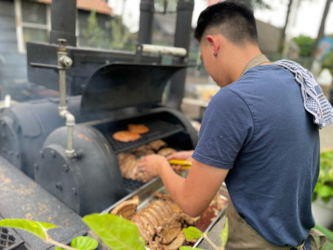 Un uomo griglia carne su un grande barbecue all'aperto a Camping Emmen, un parco vacanze a Drenthe, Paesi Bassi.