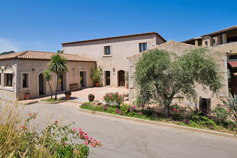 Centro Vacanze Isuledda holiday park in Sardinia, Italy, featuring stone buildings, palm trees, and flowers.