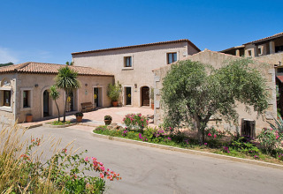Centro Vacanze Isuledda holiday park in Sardinia, Italy, featuring stone buildings, palm trees, and flowers.