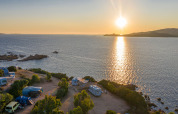Solnedgang over havet set fra Centro Vacanze Isuledda, campingvogne og telte nær vandet i Sardinien.