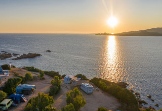 Solnedgang over havet set fra Centro Vacanze Isuledda, campingvogne og telte nær vandet i Sardinien.