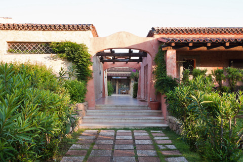 Ingang van vakantiepark Centro Vacanze Isuledda in Sardinië, Italië, met veel planten en tegels.