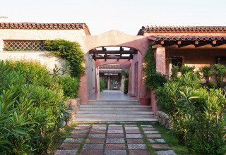 Indgang til feriestedet Centro Vacanze Isuledda i Sardinien, Italien, med grønne planter og terrasser.