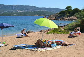 Feriegæster slapper af på en sandstrand med parasoller ved Centro Vacanze Isuledda i Sardinien, Italien.
