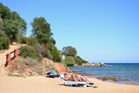Huéspedes toman el sol en la playa de arena de Centro Vacanze Isuledda, Cerdeña, Italia, junto al mar.