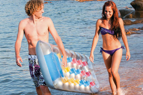 Pareja joven caminando con un colchón inflable en la playa de Centro Vacanze Isuledda, Cerdeña, Italia.