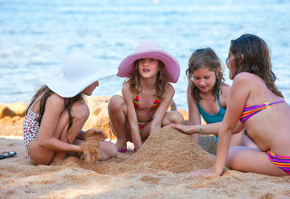 Vier kinderen bouwen een zandkasteel op het strand aan het Centro Vacanze Isuledda vakantiepark in Sardinië.