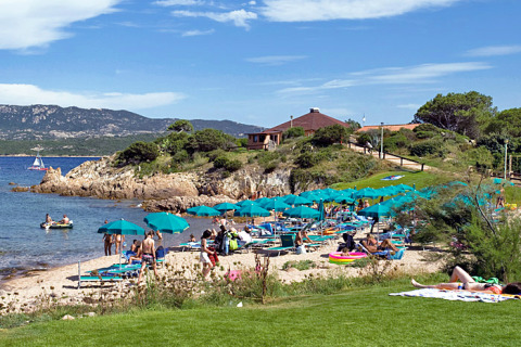 Strandscene med mennesker, parasoller og liggestole på Centro Vacanze Isuledda feriepark i Sardinien, Italien.