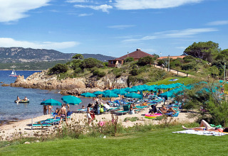 Strandscene med mennesker, parasoller og liggestole på Centro Vacanze Isuledda feriepark i Sardinien, Italien.