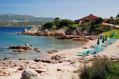 Rustig strand aan Centro Vacanze Isuledda in Sardinië, Italië, met zetels, parasols en helderblauw water.