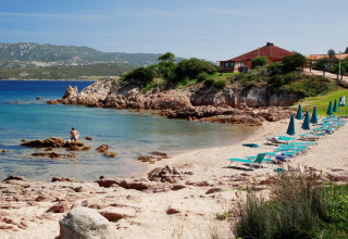Rustig strand aan Centro Vacanze Isuledda in Sardinië, Italië, met zetels, parasols en helderblauw water.
