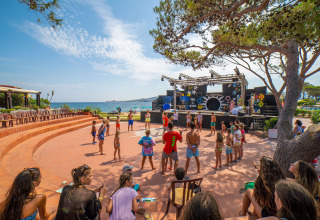 Kinderen en volwassenen genieten van buitenactiviteiten aan een podium bij de zee in Centro Vacanze Isuledda, Sardinië.