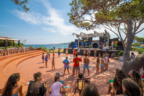Kinderen en volwassenen doen mee aan buitenactiviteiten bij een podium aan zee op Centro Vacanze Isuledda, Sardinië.