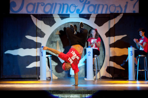 Een breakdancer voert een act uit op een podium in een vakantiepark op Sardinië, Italië, terwijl juryleden kijken.