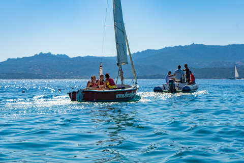 Sailboats and an inflatable boat on calm blue waters near Cannigione di Arzachena, Sardinia, Italy, with mountains.
