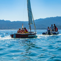 Veleros y una lancha inflable navegando cerca de Cannigione di Arzachena, Cerdeña, Italia, con montañas al fondo.