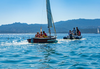 Sailboats and an inflatable boat on calm blue waters near Cannigione di Arzachena, Sardinia, Italy, with mountains.