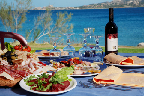 Mesa al aire libre con antipasto, vino y copas junto al mar cerca de Cannigione di Arzachena, Cerdeña.