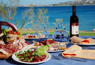 Udendørs bord med italiensk antipasto, vin og glas ved havet nær Cannigione di Arzachena, Sardinien.