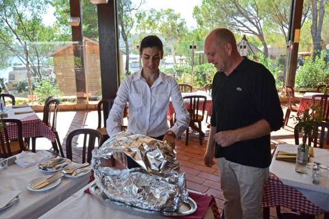 Una camarera presenta un plato cubierto con papel aluminio a un cliente en Centro Vacanze Isuledda, Cerdeña.