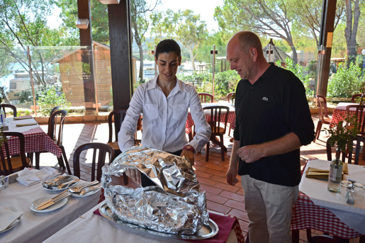 A server presents a foil-covered dish to a guest at Centro Vacanze Isuledda restaurant in Sardinia, Italy.