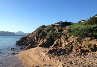 Beach view at Centro Vacanze Isuledda, Sardinia showing rocks, sea, sandy shore and people on a footpath.