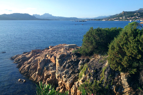 Zicht op rotsachtige kust en zee bij vakantiepark Centro Vacanze Isuledda in Sardinië, Italië, onder blauwe hemel.
