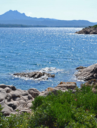 Vista costera cerca de Cannigione di Arzachena, Cerdeña, con aguas azules, rocas y montañas al fondo.