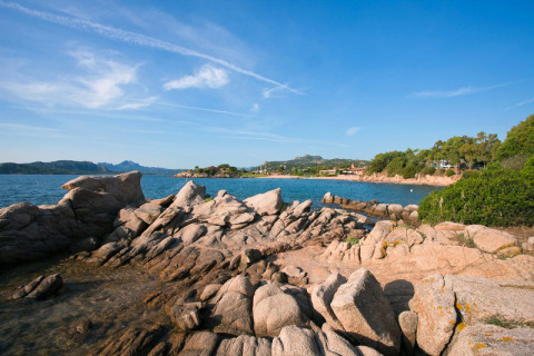 Côte rocheuse du Centro Vacanze Isuledda en Sardaigne, Italie, avec vue sur la mer et des collines verdoyantes.