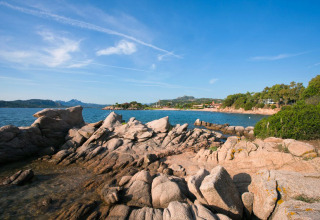 Rotsachtige kust bij Centro Vacanze Isuledda vakantiepark op Sardinië, Italië, met uitzicht op zee en heuvels.