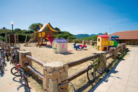Speeltuin met kleurrijke speeltoestellen en fietsen aan het hek bij Centro Vacanze Isuledda, Sardinië.