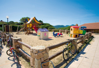 Speeltuin met kleurrijke speeltoestellen en fietsen aan het hek bij Centro Vacanze Isuledda, Sardinië.