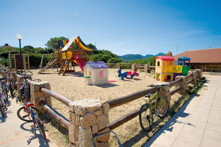 Playground with colorful equipment and bikes by a fence at Centro Vacanze Isuledda, Sardinia, Italy.