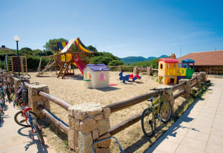 Legeplads med farverige legeredskaber og cykler ved siden af hegn på Centro Vacanze Isuledda i Sardinien.