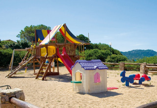 Legeplads med rutsjebane, gynge og legehus i sandet på Centro Vacanze Isuledda feriepark i Sardinien, Italien.